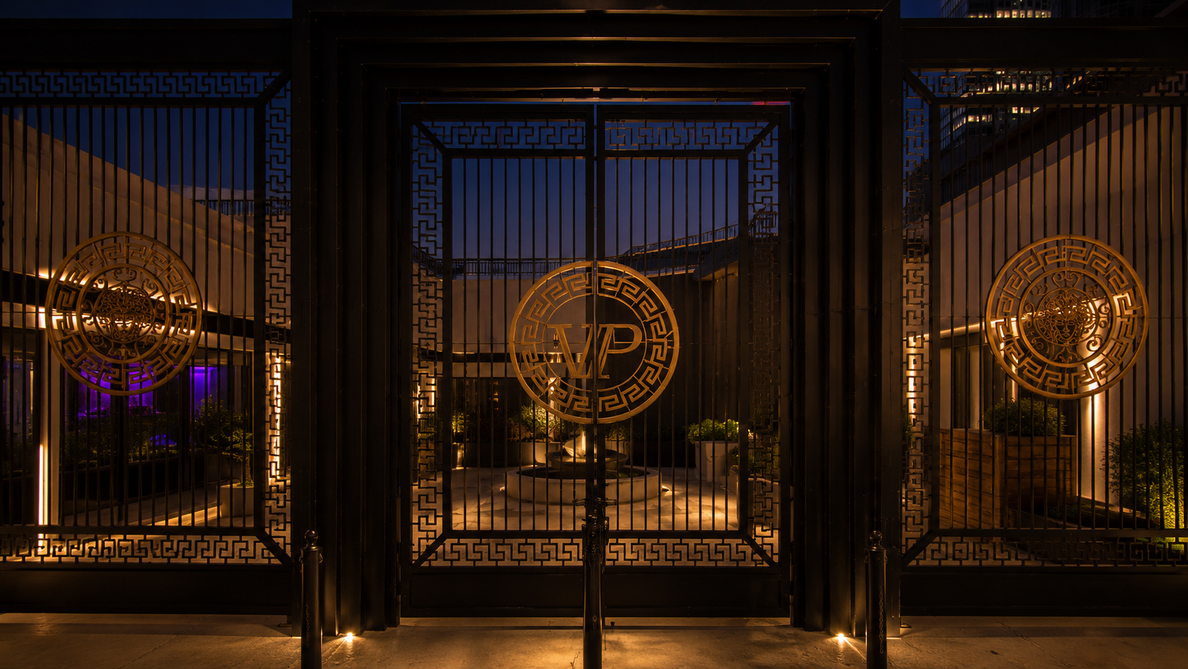 Vice Park Dallas entry gates with illuminated brass VP medallion on ornate ironwork